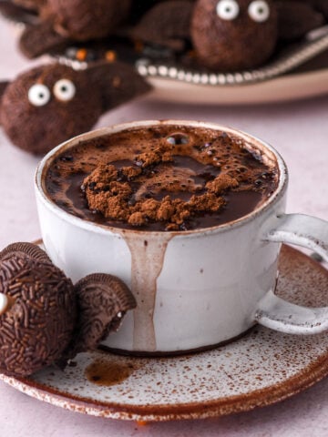 No-Bake Chocolate Halloween Truffle shown next to a cup of hot chocolate. There are more truffles in the background.